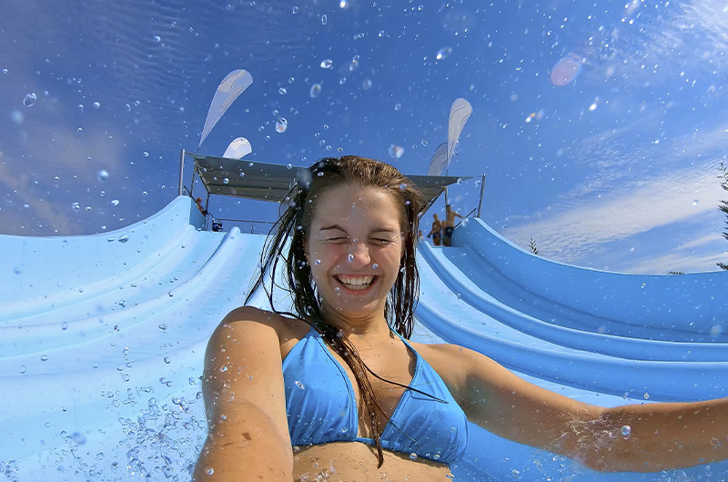 Mujer deslizándose por un tobogán azul en Aquamijas, disfrutando del verano en el mejor parque acuático de Andalucía.